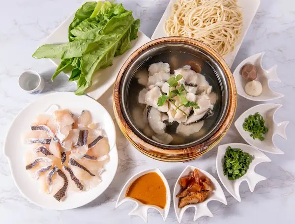 Fish noodle soup pot served with sliced fish, fresh greens, noodles and dipping sauces