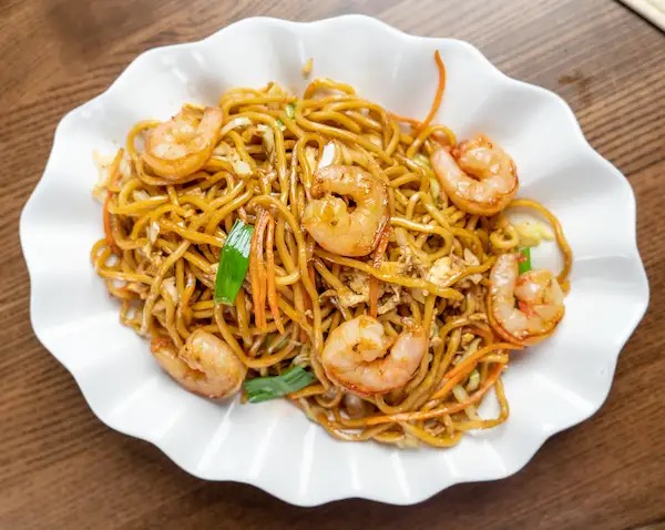 Prawn chow mein with shrimp, carrots and scallions on a scalloped white plate