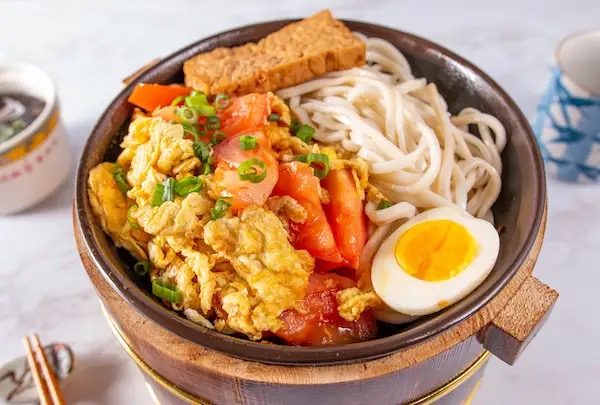 Tomato and egg mixed noodles with scallions in a wooden bowl